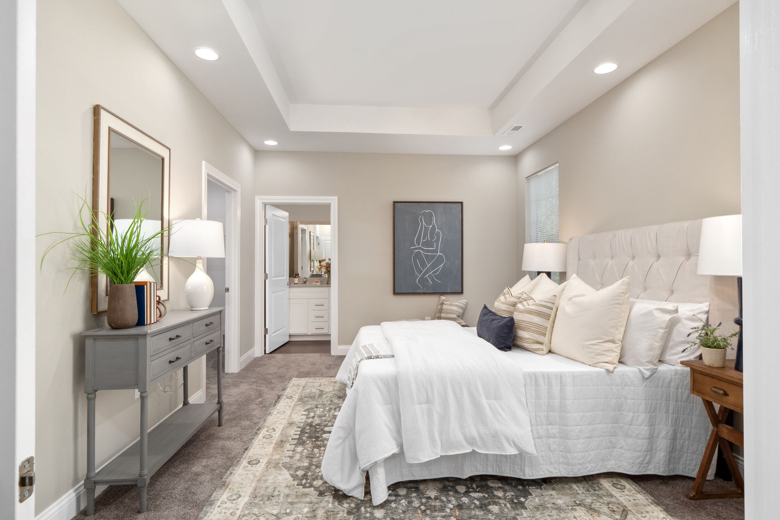 A large bedroom with plush carpet, a window, recessed lighting, and access to a private bathroom.