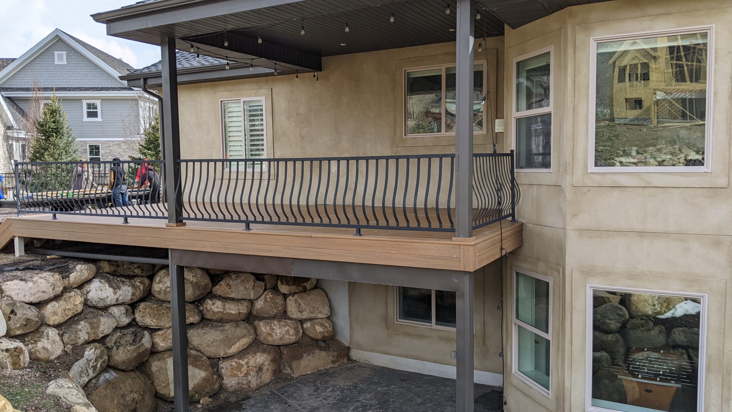 Expand your outdoor living possibilities with this extensive multi-level deck from DeckPro LLC. This custom design features a large upper composite deck area with sophisticated, dark curved metal railings, providing an elevated space for entertaining. Wide, built-in steps lead down, following the natural slope of the landscape to connect with the lower concrete patio, creating a cohesive, functional space that integrates beautifully with the surrounding rock retaining walls.