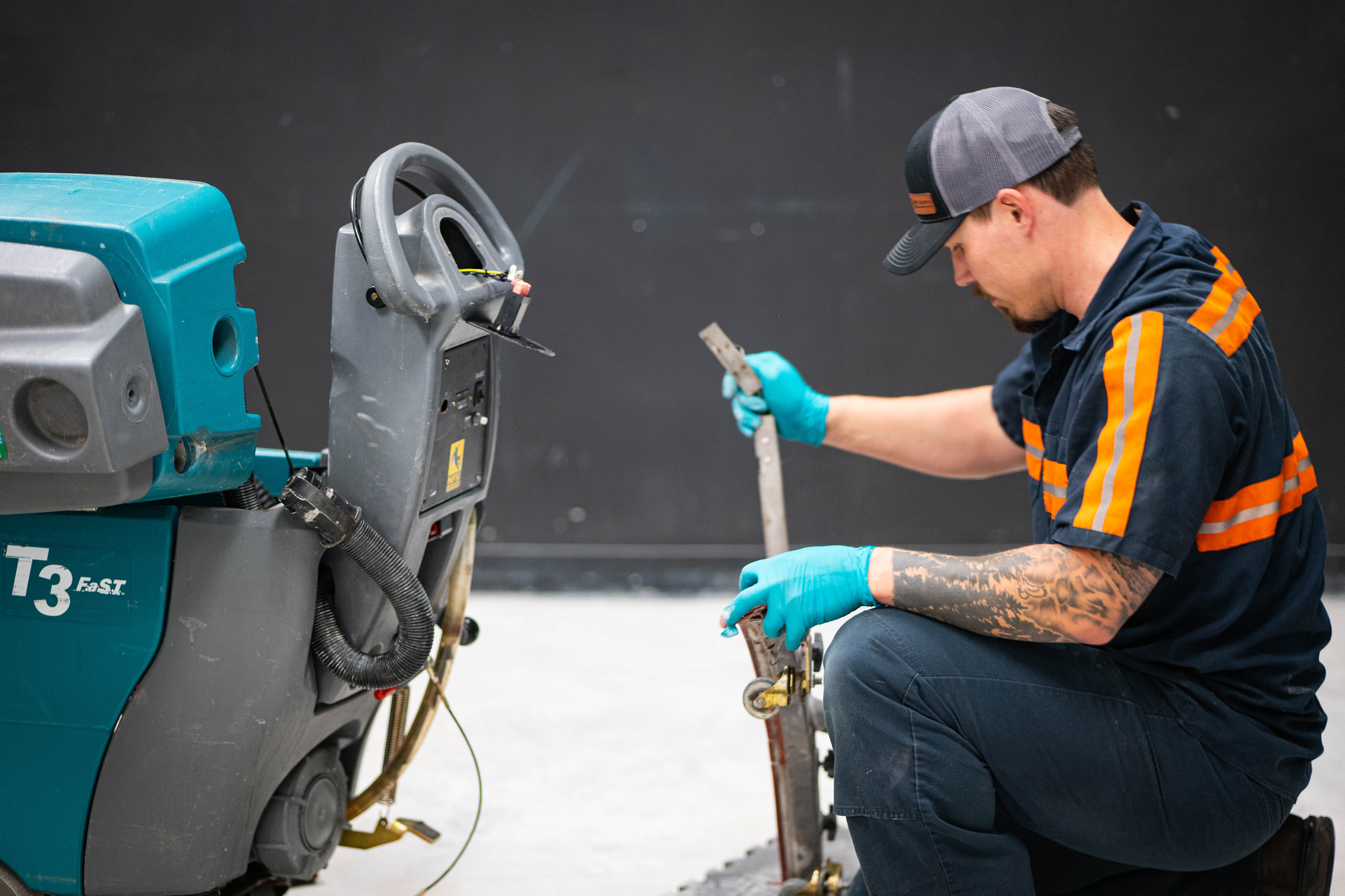 A certified WaySolutions technician inspects and cleans the rear squeegee tool assembly of a teal Tennant T3 FAST walk-behind floor scrubber. Serving commercial facilities across Layton, Utah, our team performs essential water recovery maintenance and wear-part replacements to guarantee perfectly dry, slip-free floors.