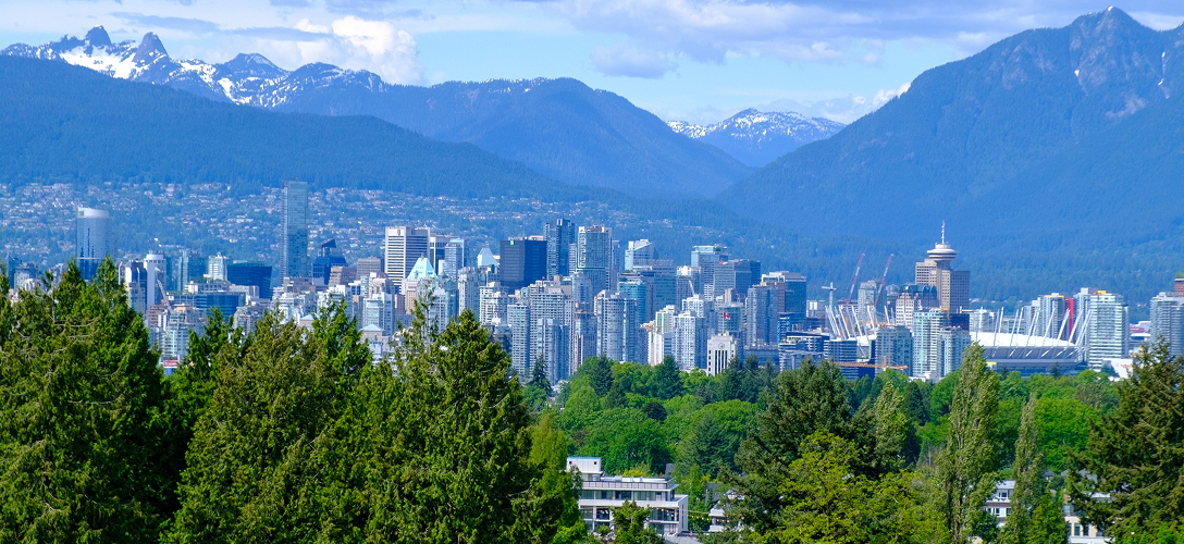 Vancouver city skyline as seen from afar, with mountains in the background.