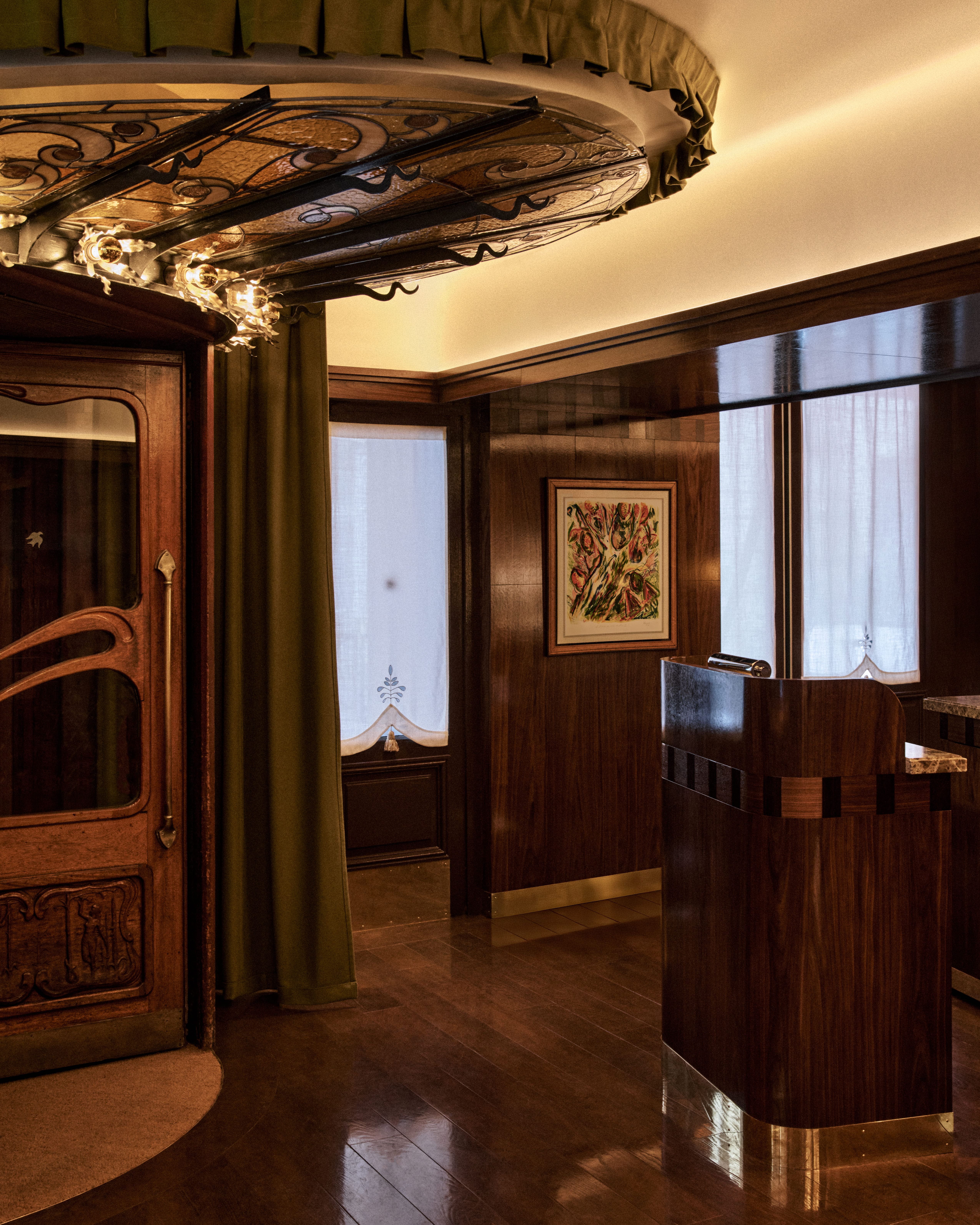 Art Deco–style restaurant entry with curved wood host stand, stained-glass canopy, and warm walnut paneling.