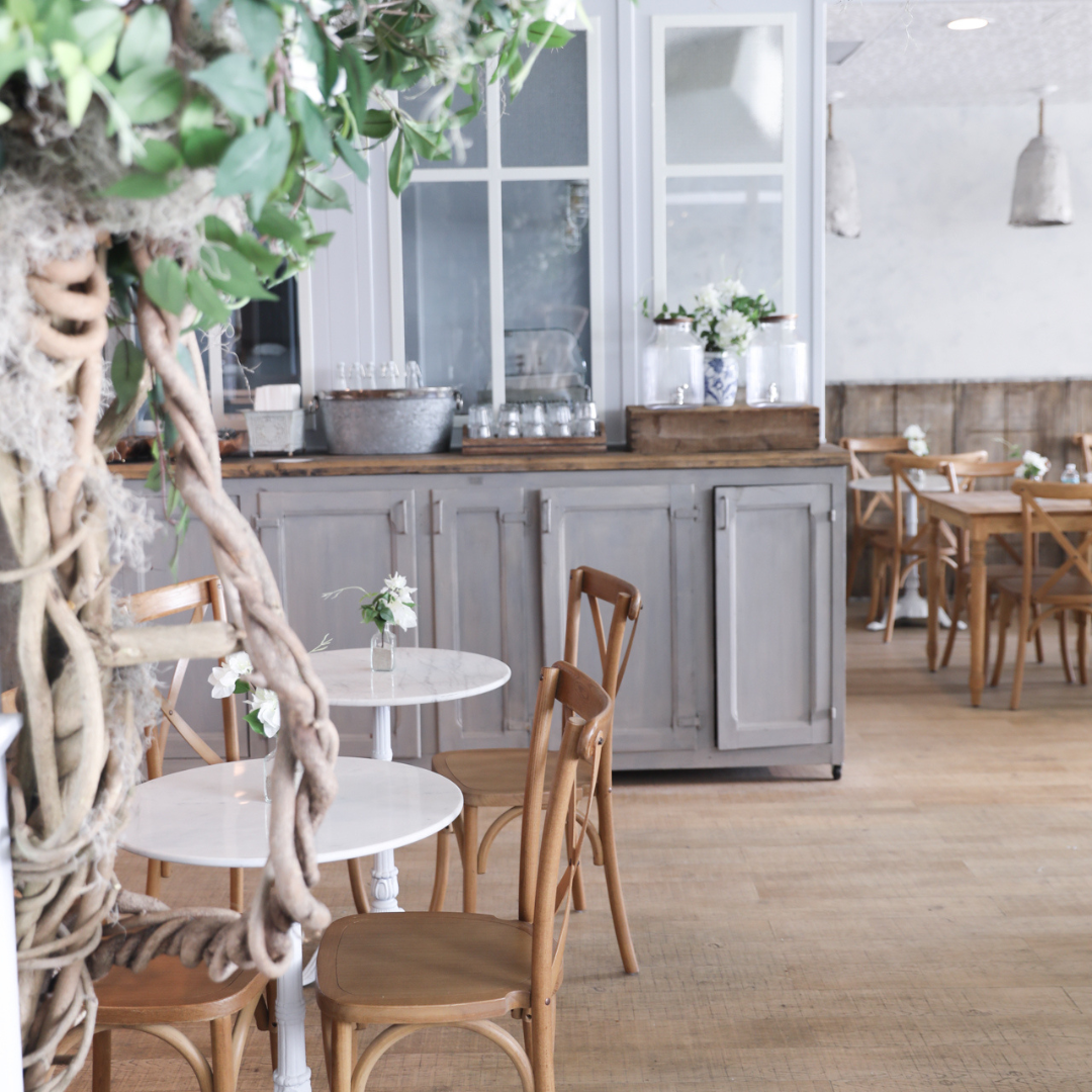 Twisting branches and leafy greenery frame the dining room, where natural textures, soft neutrals, and simple floral arrangements create a calm, garden-inspired atmosphere.