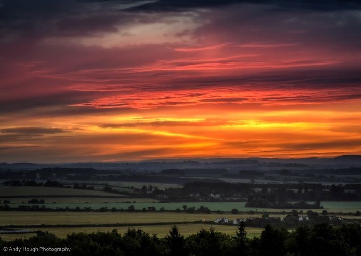 A colourful sunrise breaking through dark sky on a cloudy morning.