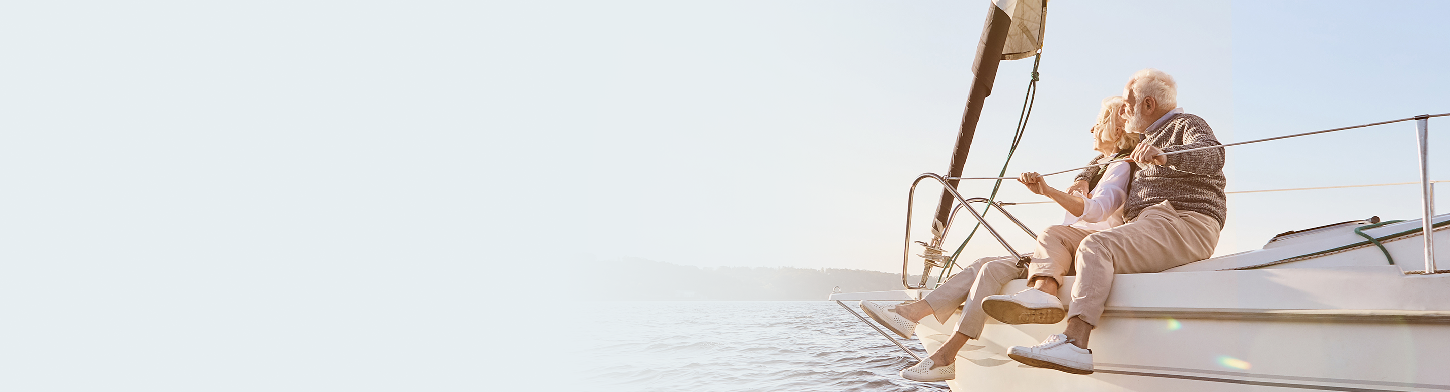 An elderly couple sitting on the bow of a boat with their legs hanging down.