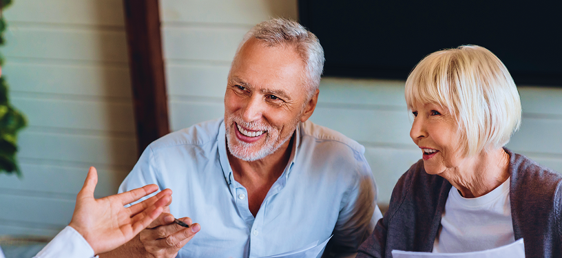 An elderly couple speaking to an advisor while reviewing papers at a table.