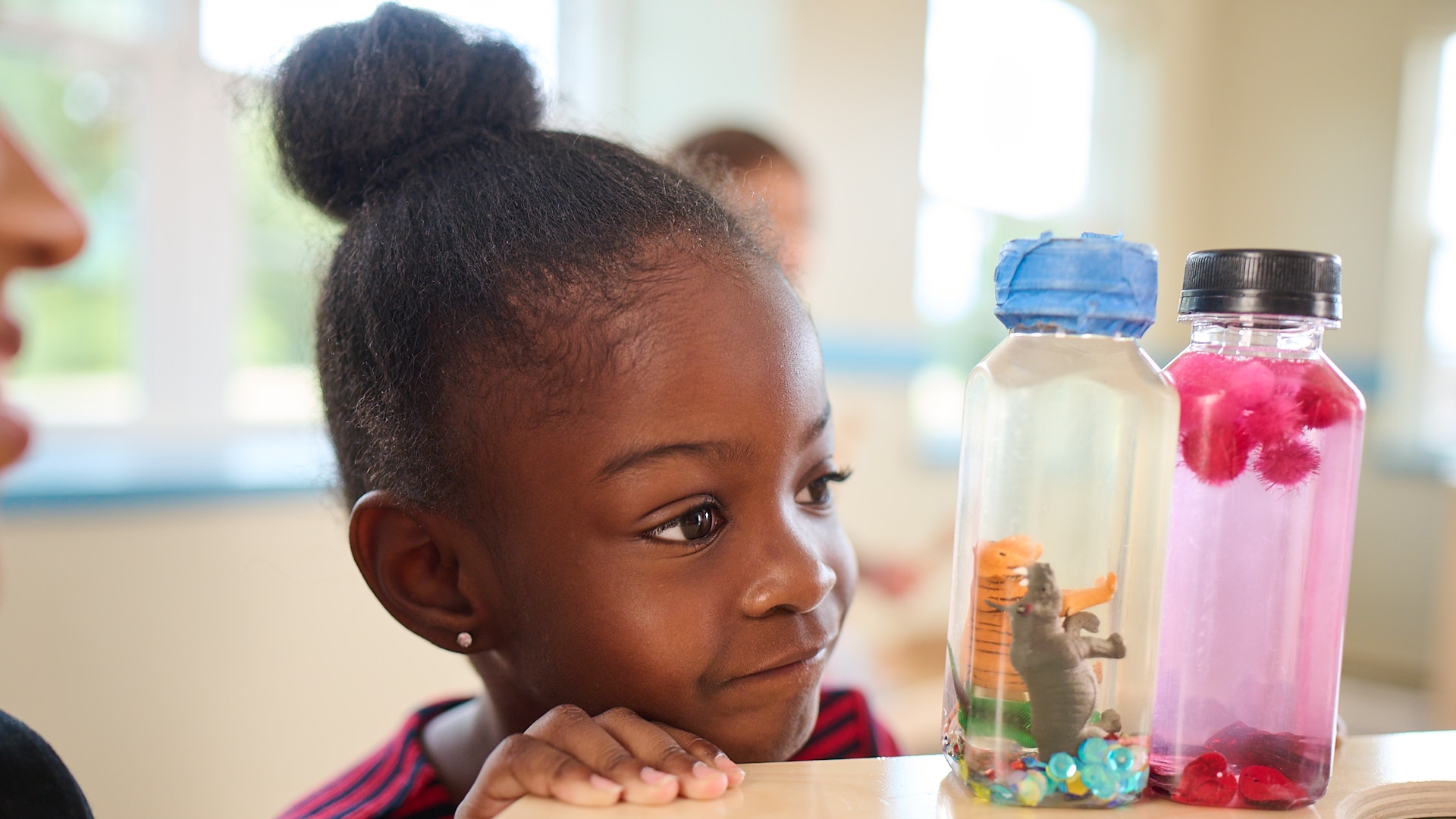 Primrose Schools preschool girl curiously observing sensory discovery bottles during science exploration activity