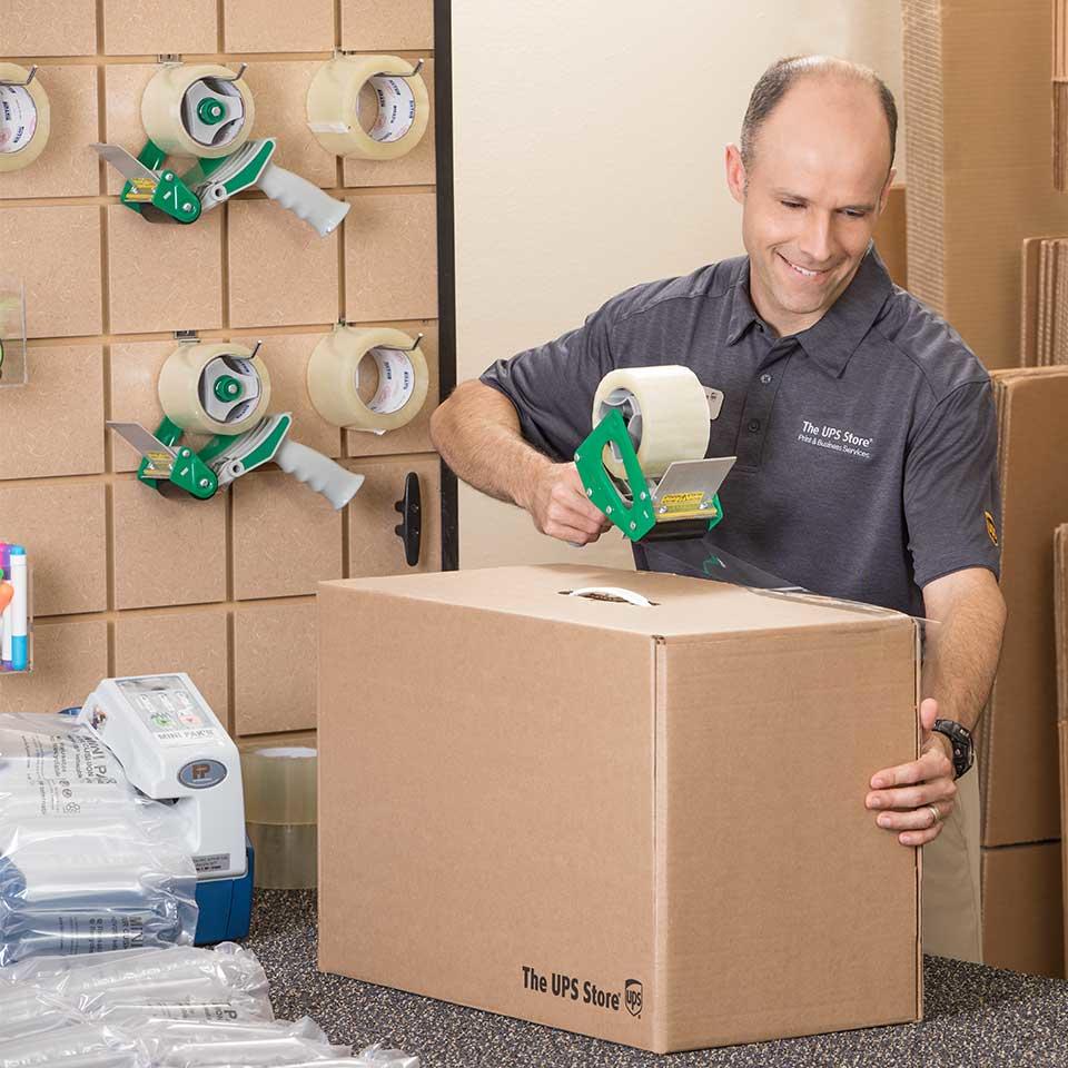 El franquiciado de The UPS Store poniendo cinta a una caja de envío