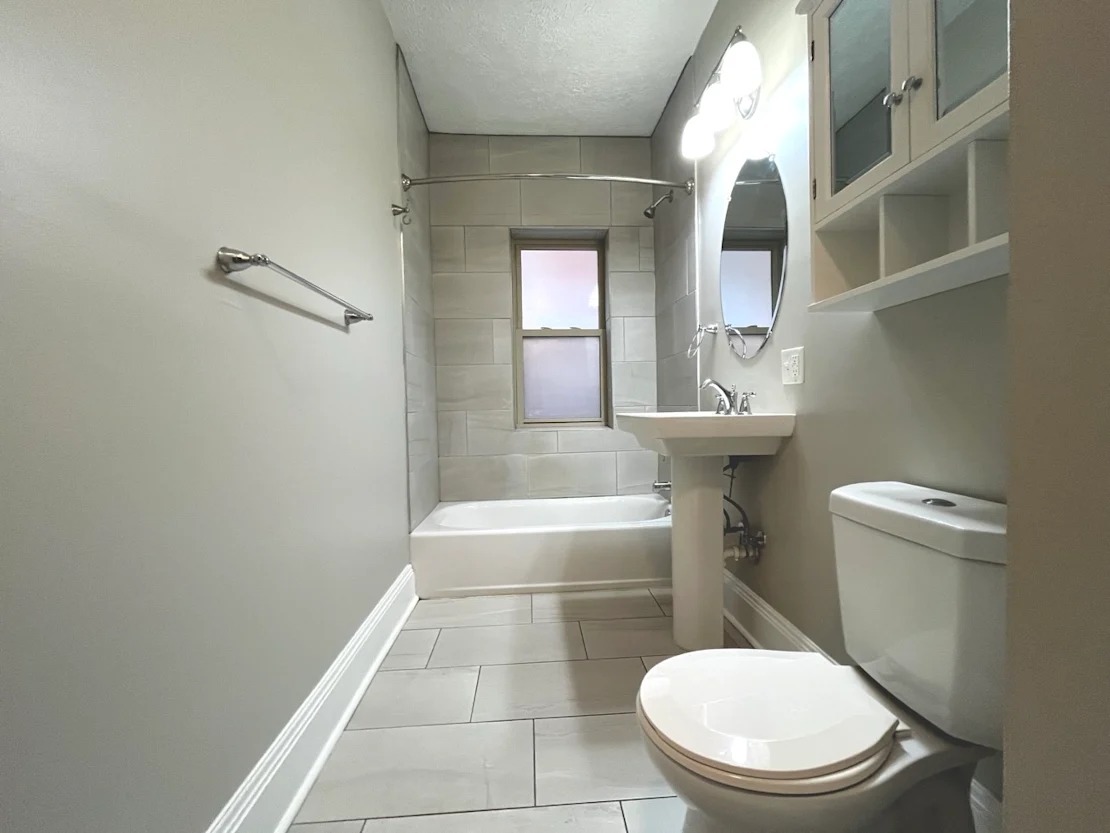 A white toilet sits in a bathroom with a white sink and a white bathtub.