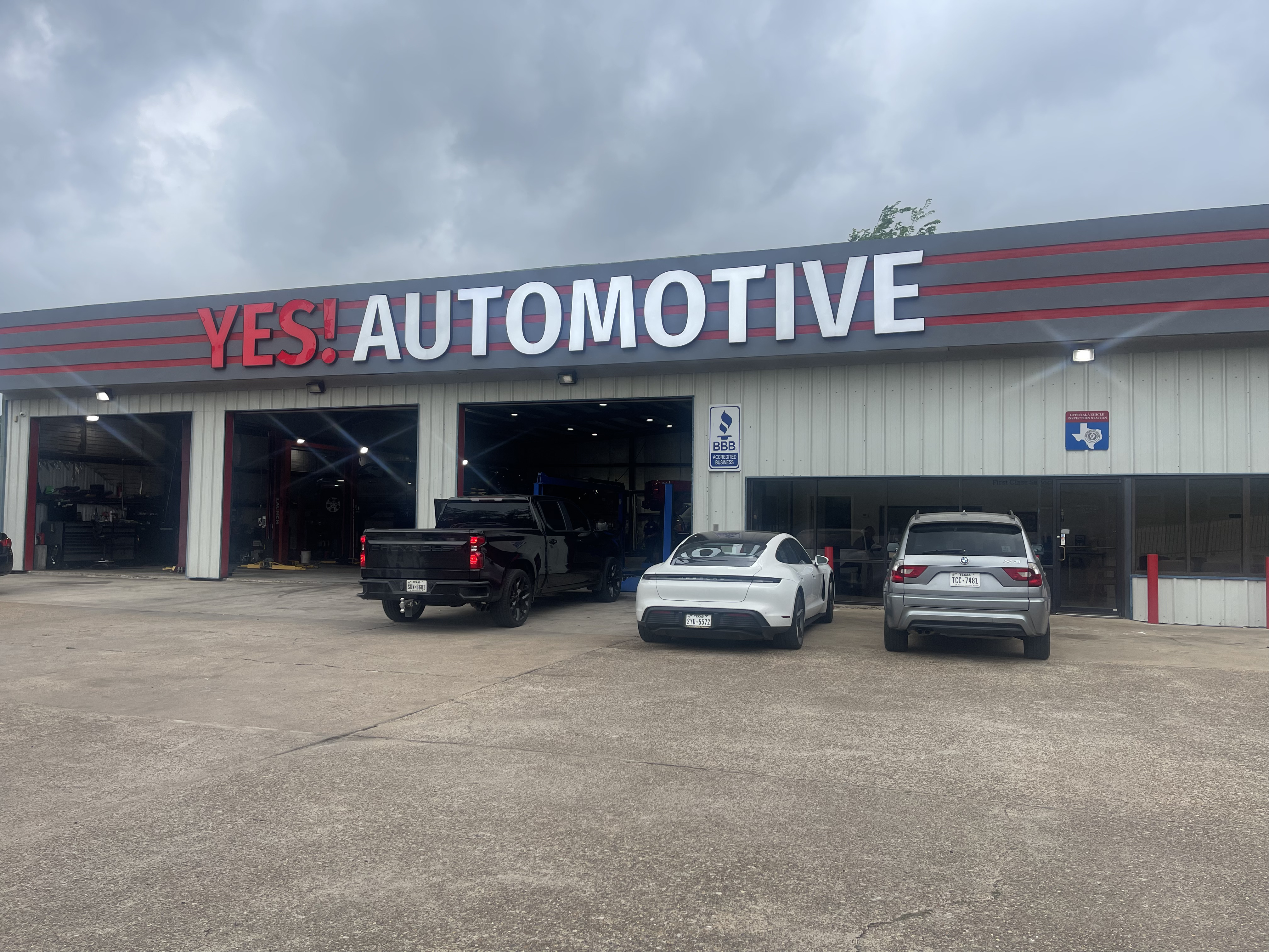 Front exterior view of YES! Automotive in Porter, Texas, featuring prominent red and white signage, multiple open automotive service bays, a spacious parking area, and vehicles parked outside. The facility offers professional auto repair, transmission repair, diagnostics, and routine vehicle maintenance.