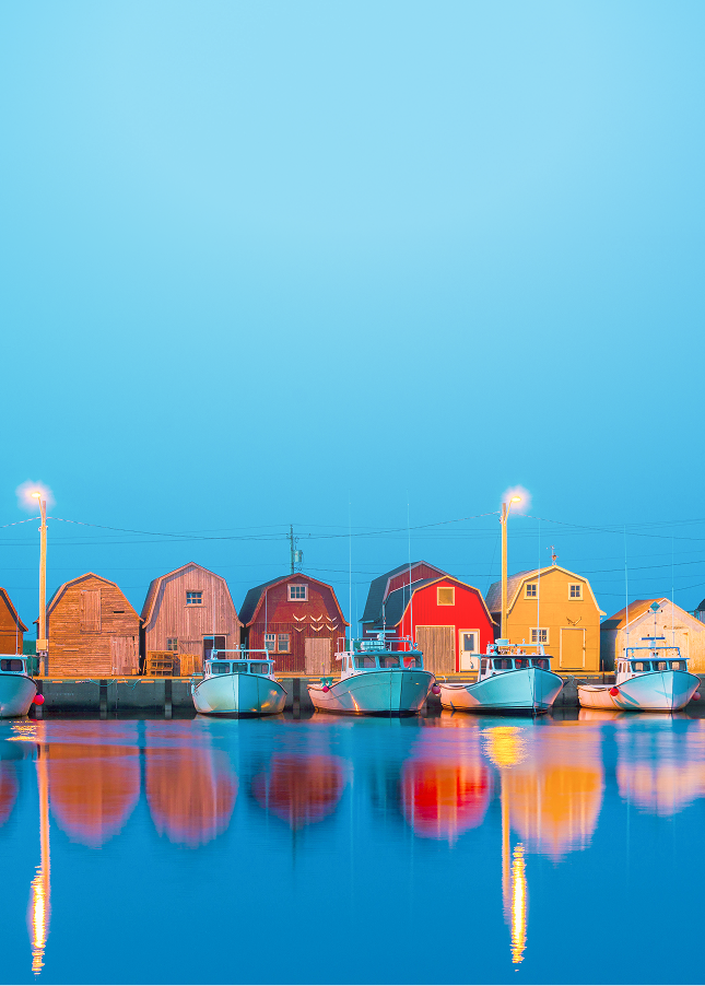 Charming row of docked fishing boats and fishing sheds during blue hour at Malpeque Harbour, Prince Edward Island.