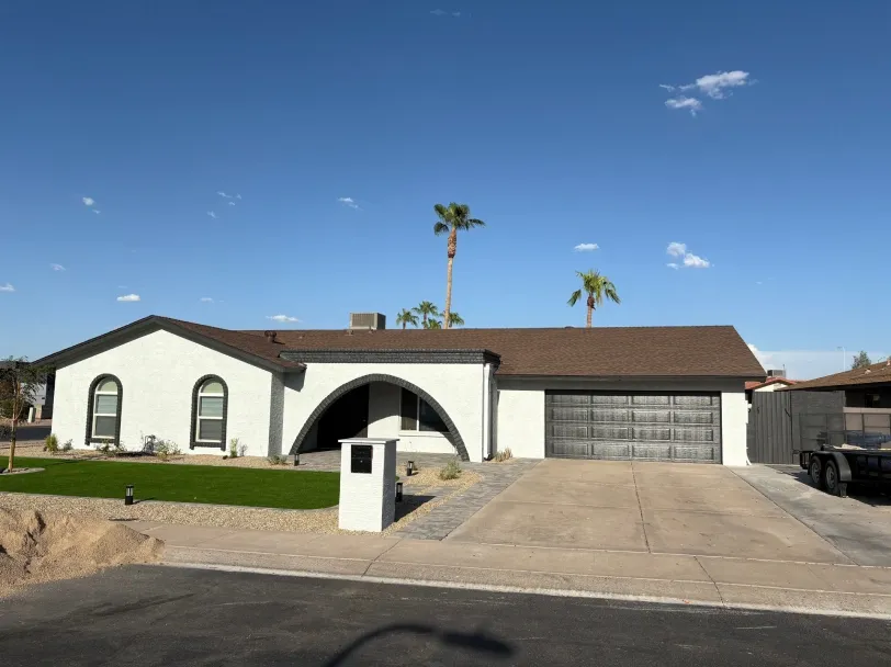 Freshly painted single-story home with white exterior, brown roof, arched entryway, and double garage, featuring a clean driveway, landscaped yard, and palm trees under a bright blue sky.