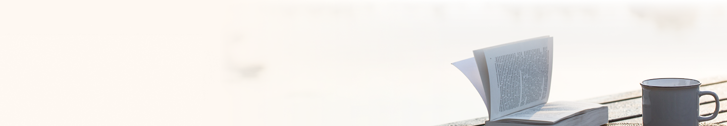 An open book next to a coffee mug on an outdoor table.