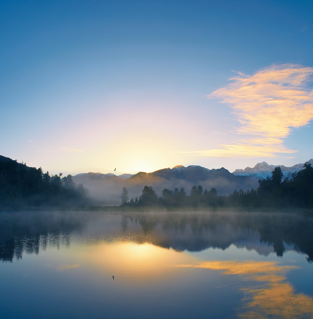 A calm lake setting with reflections of the sun and clouds in the water.
