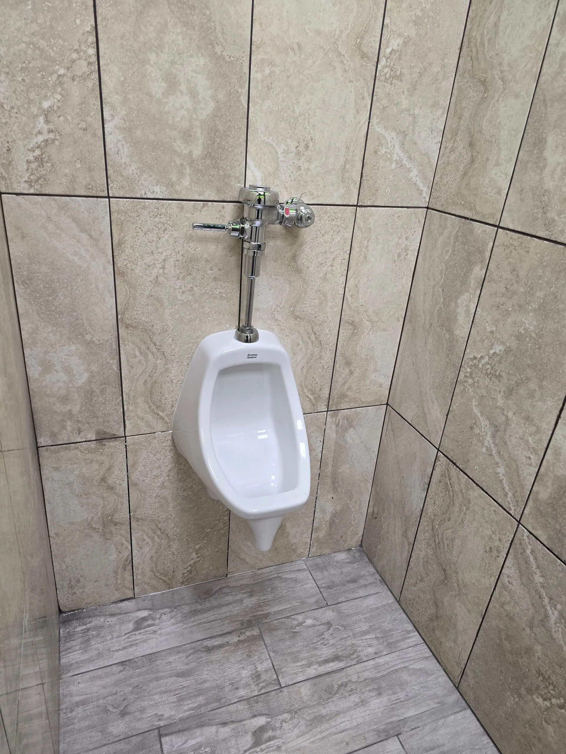 Professionally installed commercial wall-mounted urinal with chrome flush valve and tiled restroom demonstrates quality plumbing fixture installation, durable construction, hygienic design, and dependable commercial restroom plumbing solutions available.