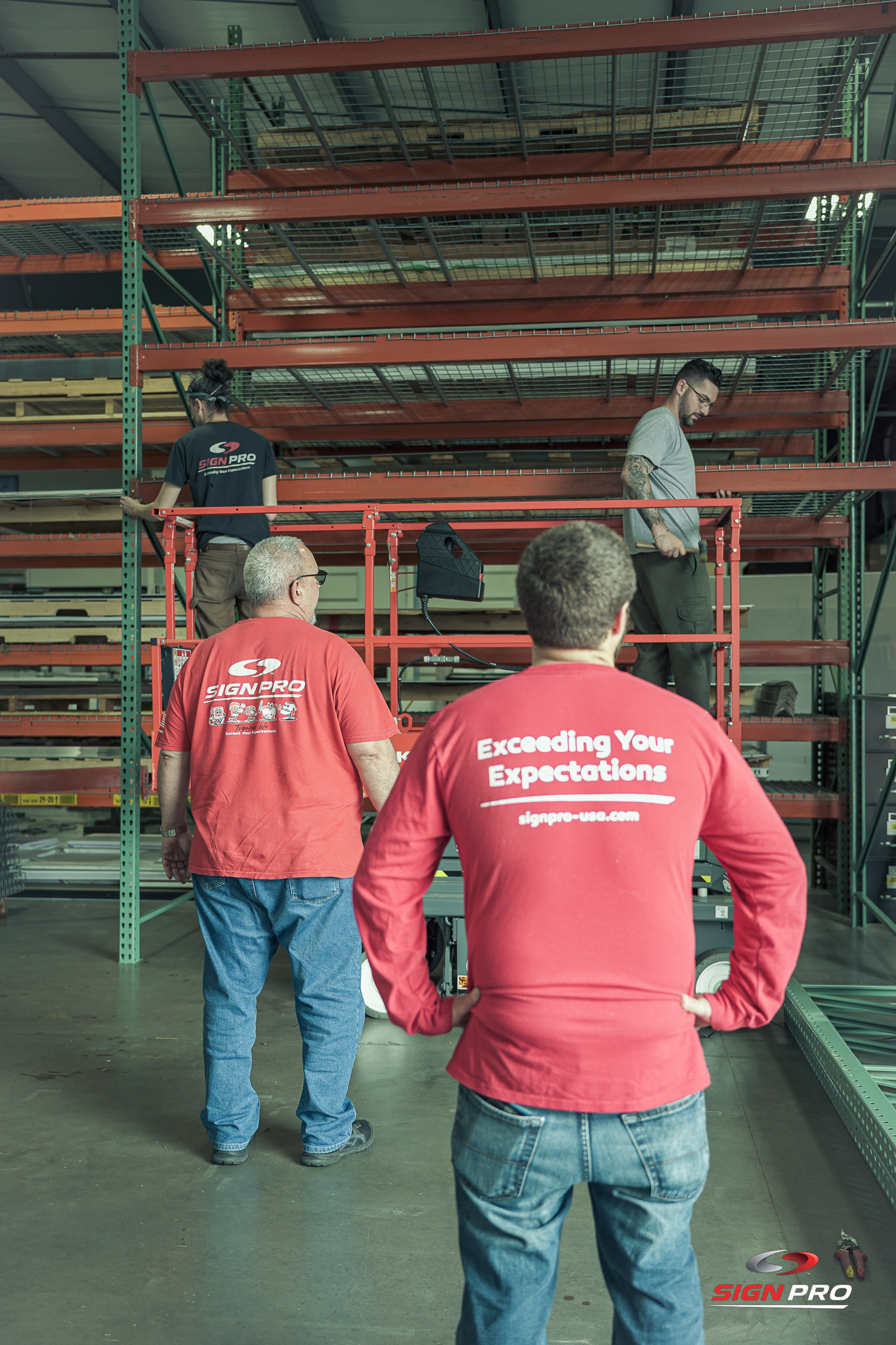 Sign Pro, Inc. team members working together in the warehouse facility, demonstrating teamwork and operational efficiency in handling large-scale sign production materials.