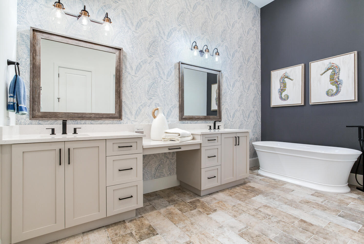 Coastal-style bathroom with a double vanity, framed mirrors, marble-look tile flooring, and a decorative accent wall.
