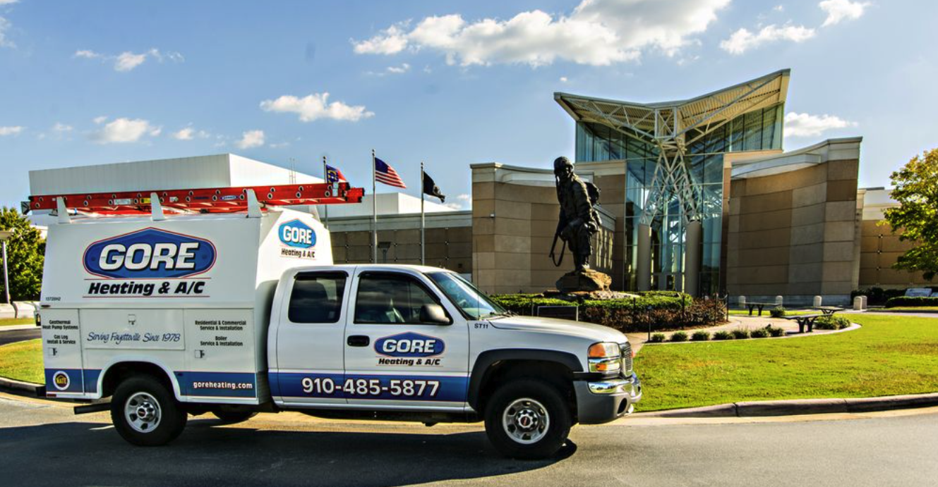 A branded Gore Heating & A/C INC company truck is parked in front of a commercial building offering commercial services. The truck is unoccupied and prominently displays the company's logo and contact information. Its clean exterior and well-maintained appearance reflect the company's professionalism and commitment to quality service
