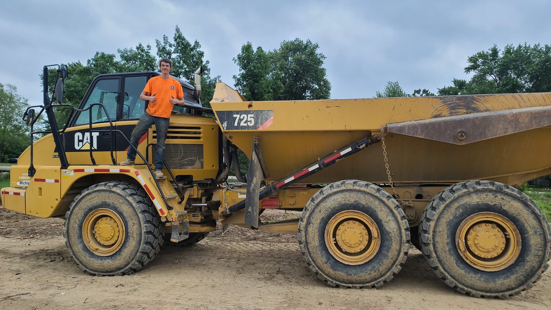 A construction worker poses beside a Caterpillar articulated dump truck used for hauling soil and aggregate. The machine supports large-scale excavation and earthmoving operations.