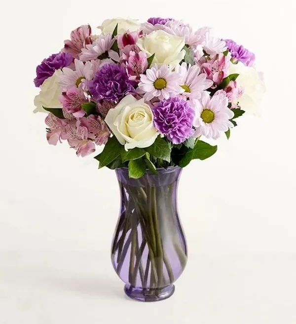 A beautiful bouquet of white roses, purple carnations, and pink alstroemeria flowers arranged in a p 