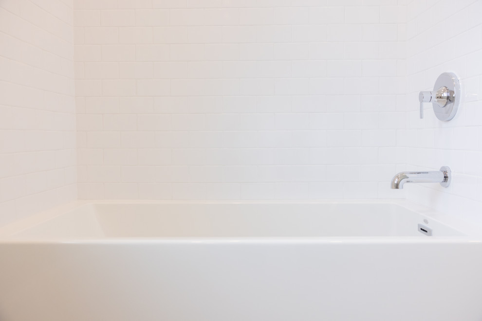 A white bathtub with white subway tile walls and chrome fixtures. The image shows a clean and modern bathroom setting.