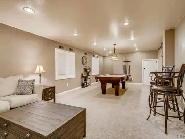 Spacious basement recreation room designed for entertainment, featuring a pool table, comfortable seating, neutral wall colors, recessed lighting, and open floor layout ideal for gatherings and family activities.