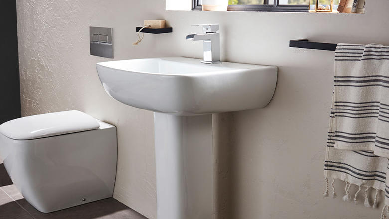 A white modern basin on a pedestal with silver mixer tap in a cream tiled bathroom