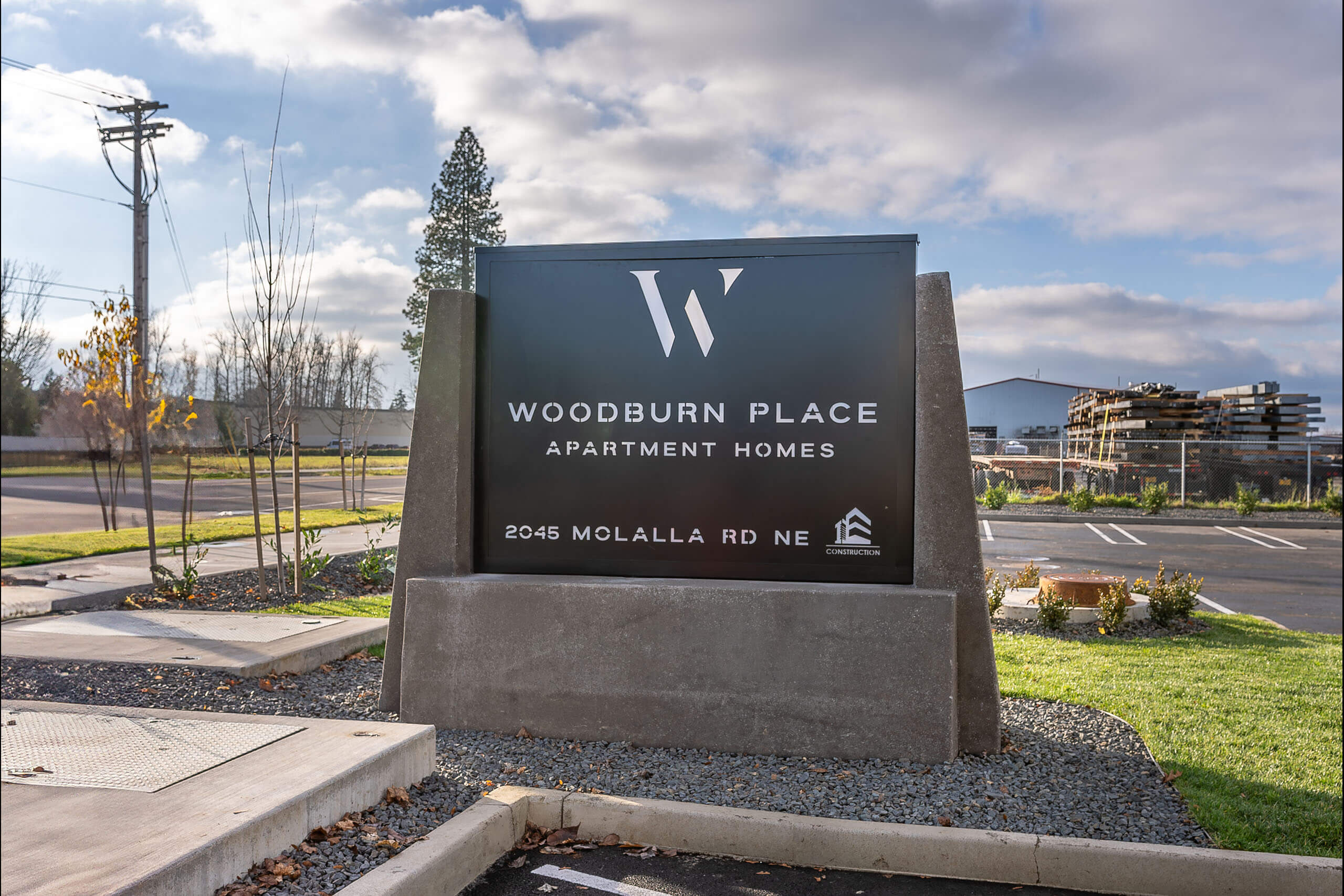 A sign for Woodburn Place Apartment Homes stands in front of a parking lot.