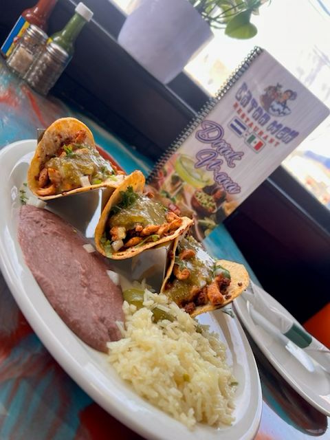 Three chicken street tacos topped with salsa verde and served with Mexican rice and refried beans at Catramex Restaurant.