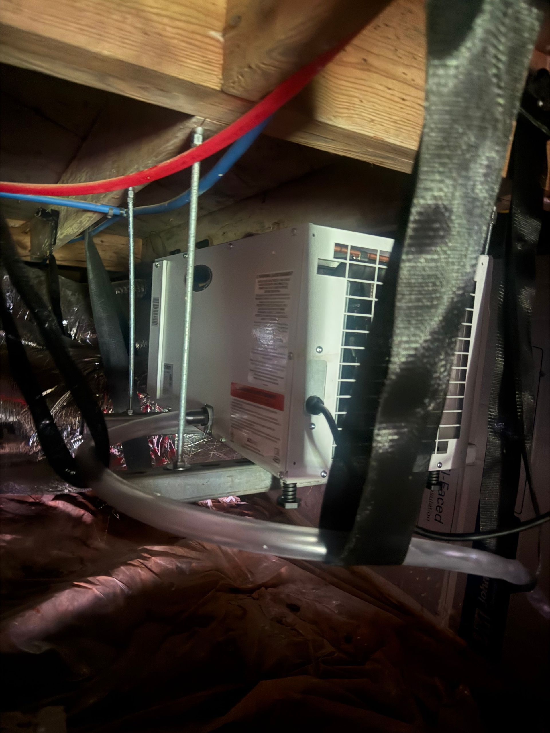Compact HVAC equipment installed in an attic or crawlspace, surrounded by insulated ducts, flexible  