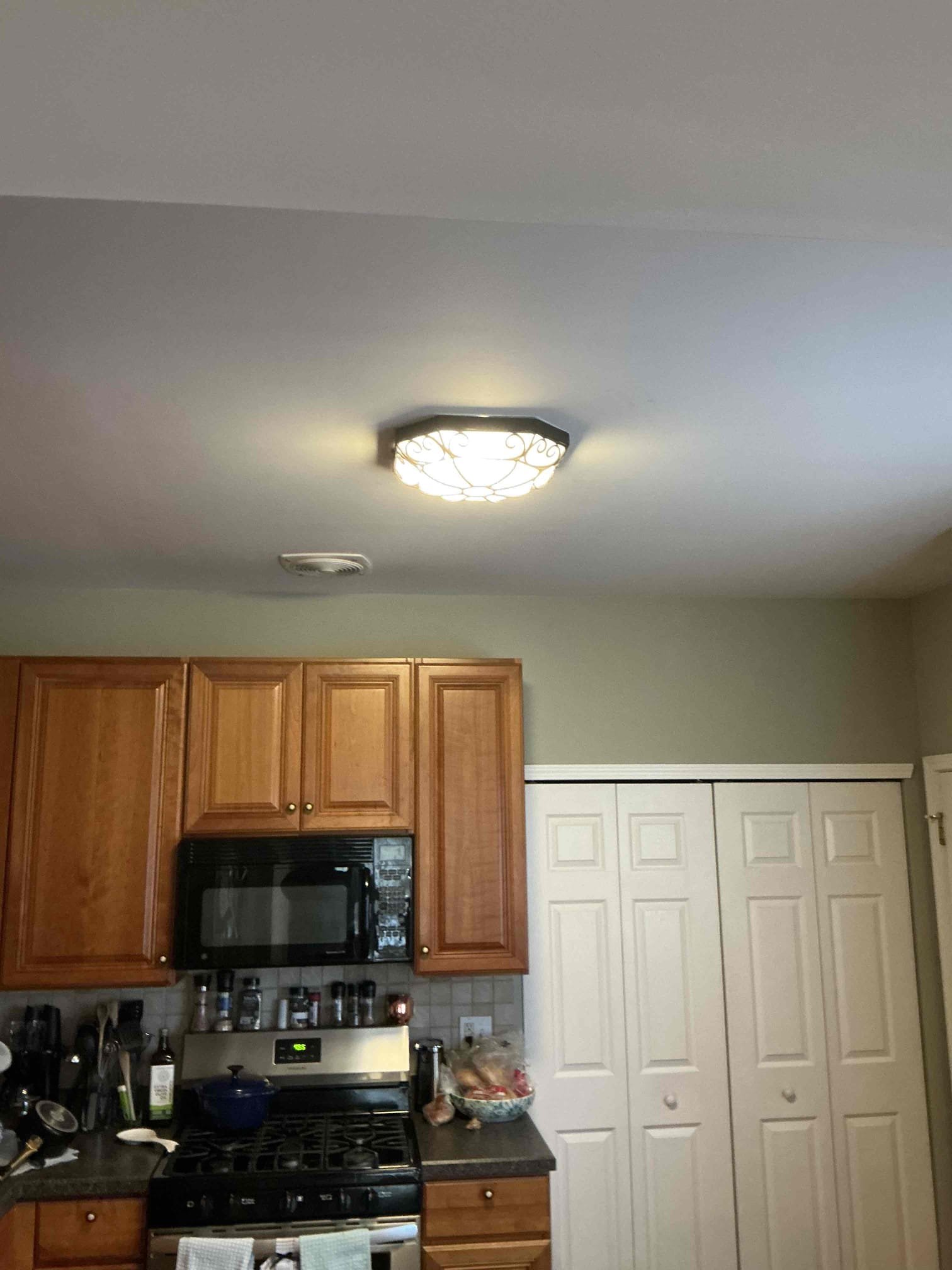 A decorative flush-mount ceiling light with a scrollwork glass shade installed by Thomas Edison Electric in a Southampton, PA kitchen. The fixture provides warm overhead lighting for the cooking and prep area.