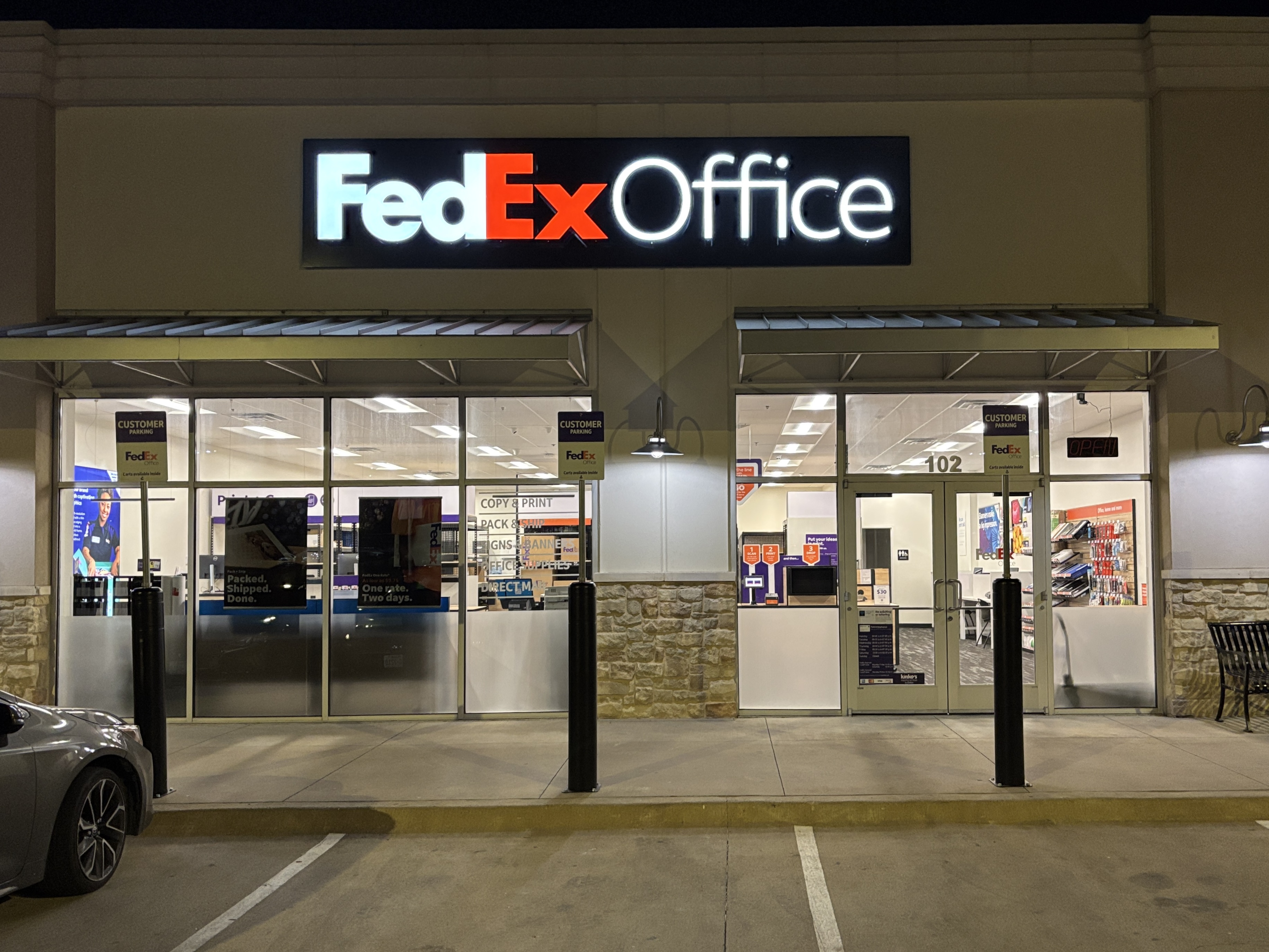 The illuminated storefront and main entrance of the FedEx Office in Temple, TX, viewed from the parking lot at night.