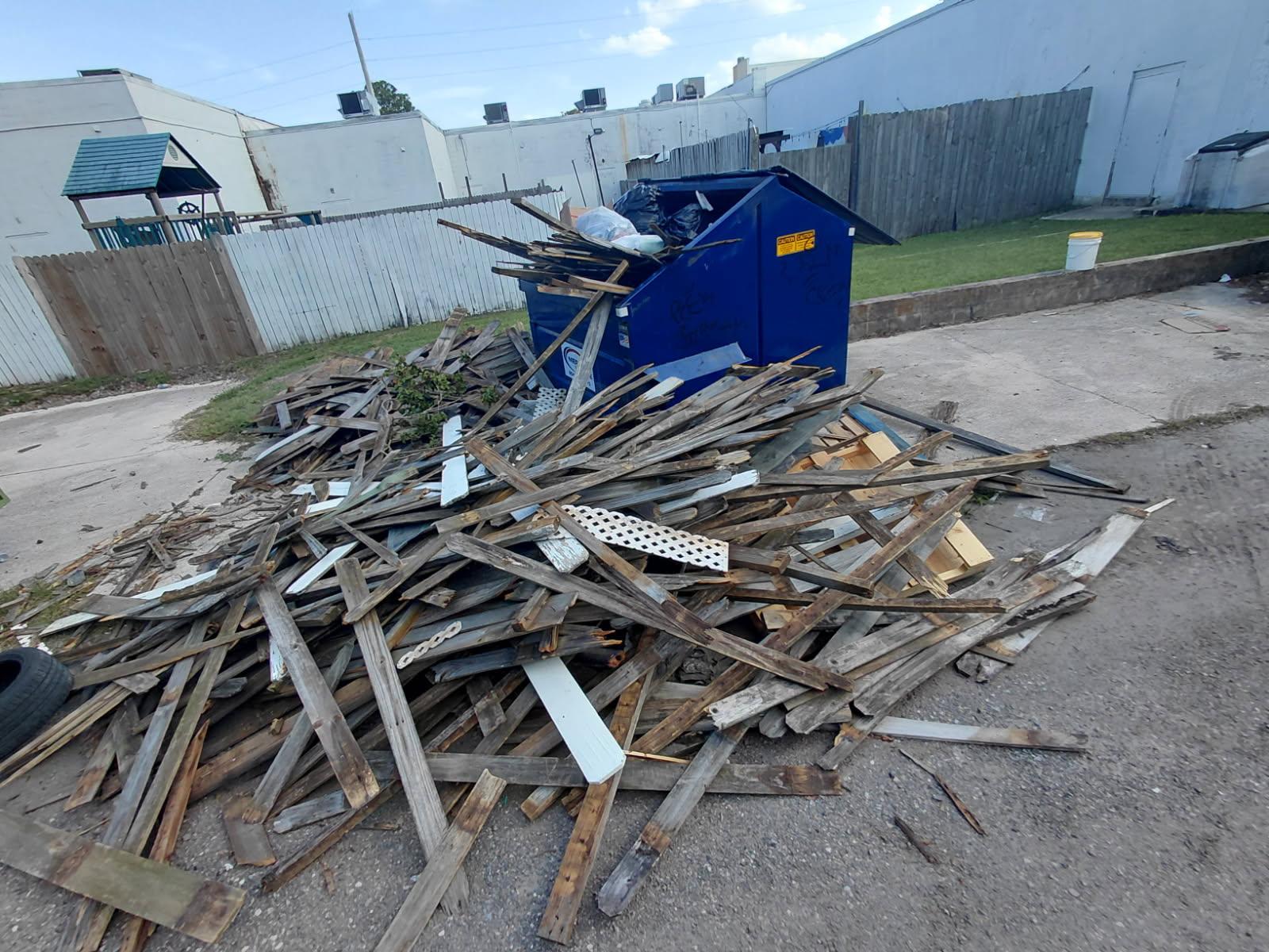 A large, scattered pile of broken wooden boards and lattice debris piled on the ground surrounding a 