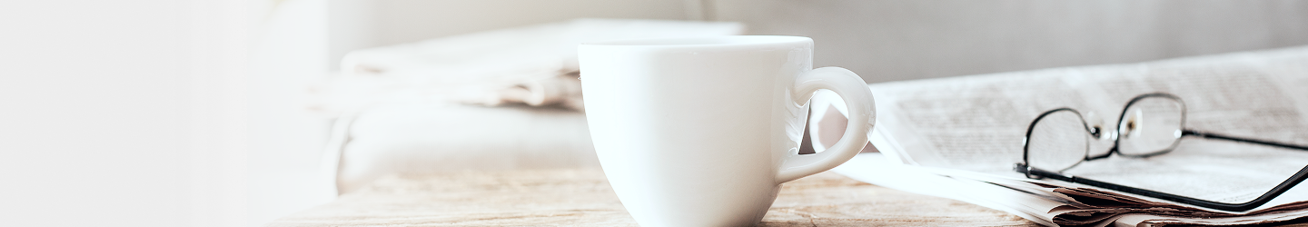 Un bureau avec un journal, une tasse et une paire de lunettes dessus.