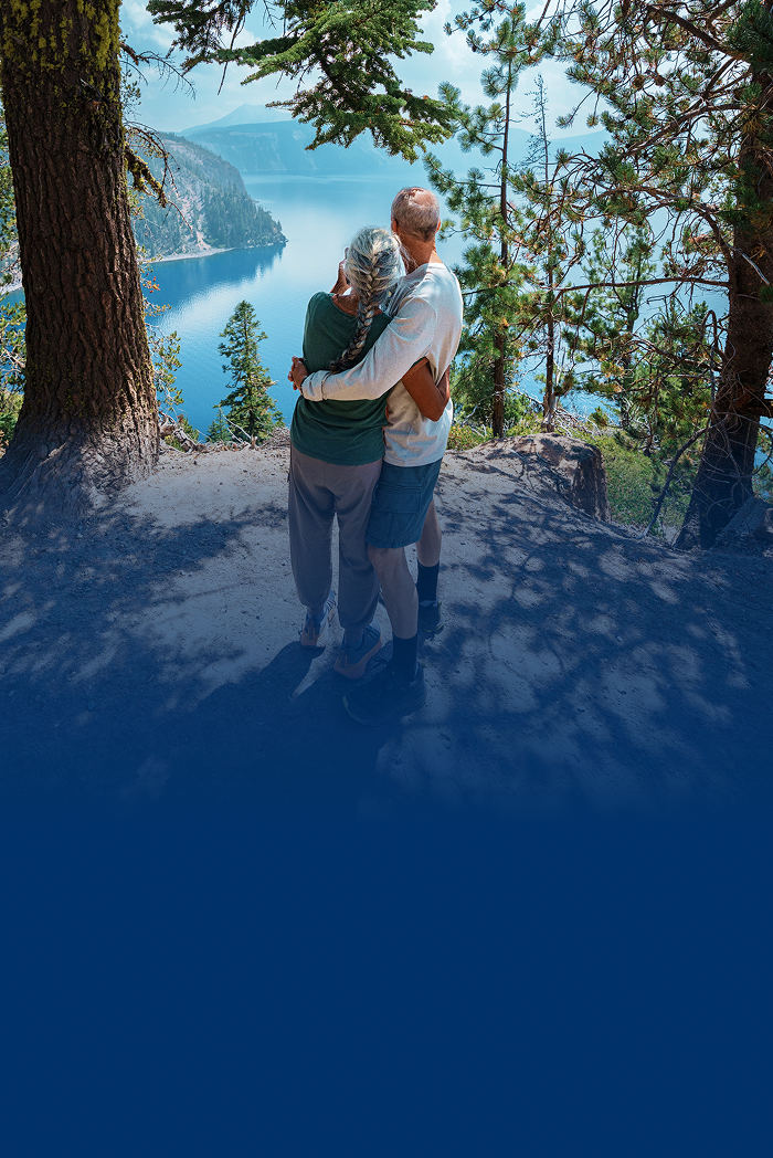 An older couple embracing while enjoying a lake and mountain view.