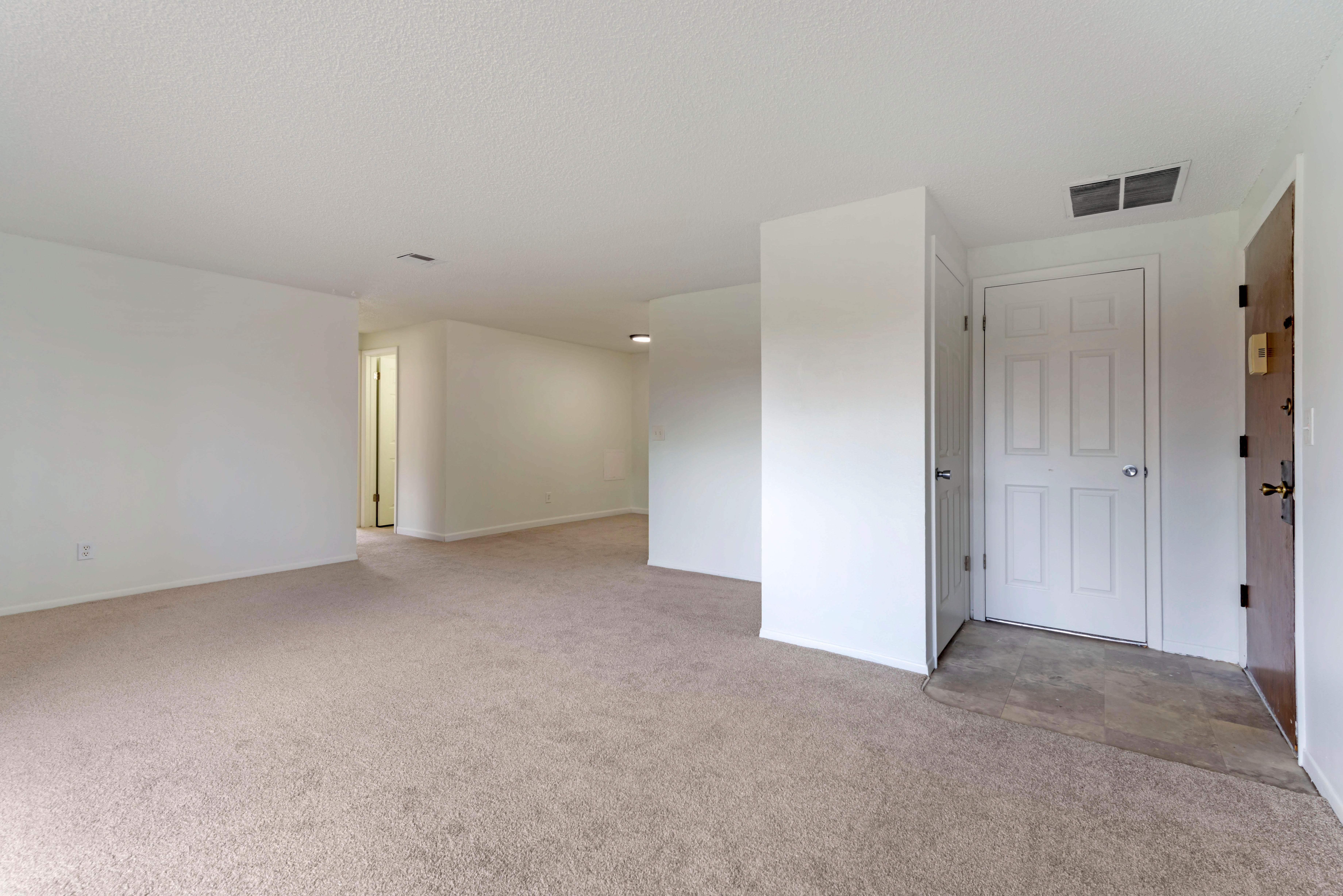 Tile entry with view to carpeted living area, dining area, and hallway to bedrooms.