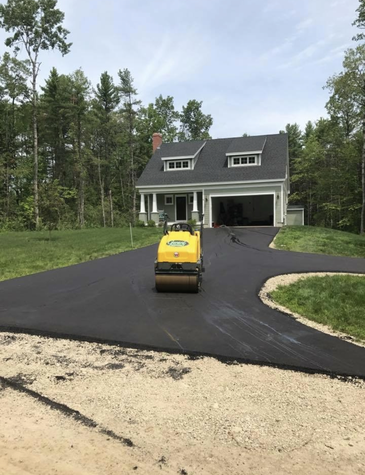 Residential driveway compaction in progress using a roller, ensuring a strong, long-lasting asphalt surface.