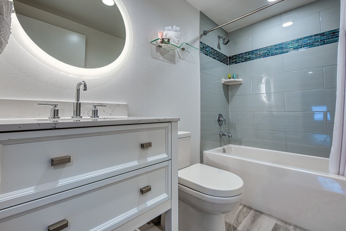 Updated guest bathroom with illuminated mirror, modern vanity, and full bathtub at FUSION Resort in Treasure Island, Florida.