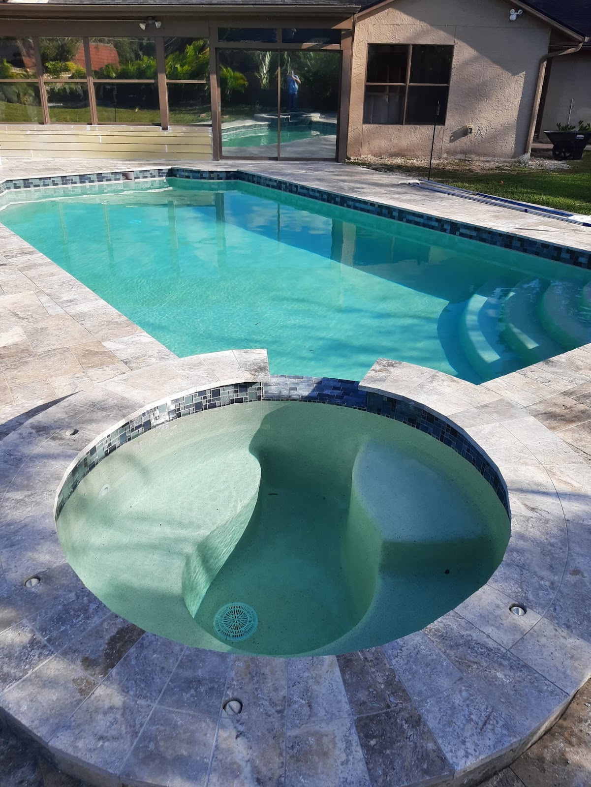 Residential backyard swimming pool with an attached round spa, light stone paver decking, and a screened outdoor area.