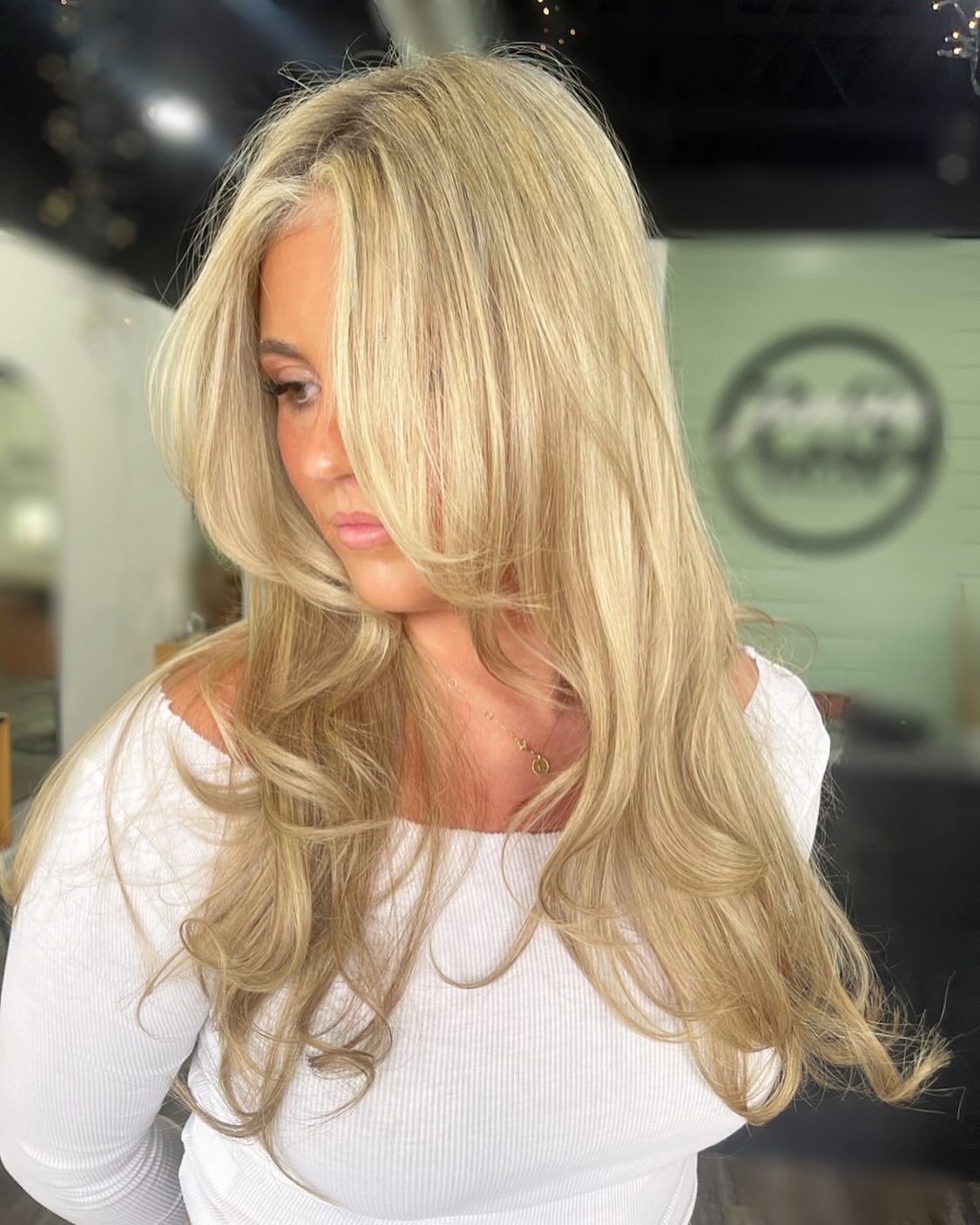 Woman with long voluminous blonde hair styled in soft layers and curls, photographed indoors inside a modern hair salon.