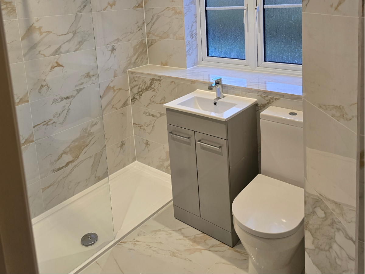 Compact bathroom with marble-effect wall tiles, vanity unit, toilet, and natural light from window.