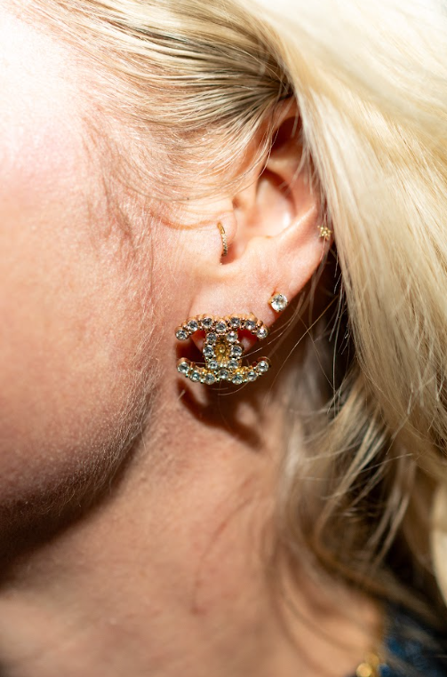 A gold-toned interlocking logo earring with sparkling stones pairs with a clear stud and small star accent. Explore statement earrings and curated jewelry at Eliana Curated in Old Town Alexandria, VA.