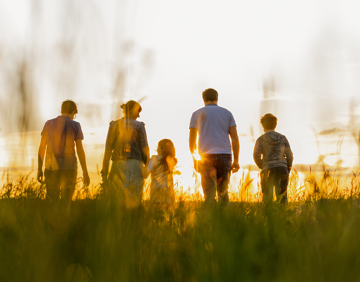A multigenerational family standing in a field at sunset.