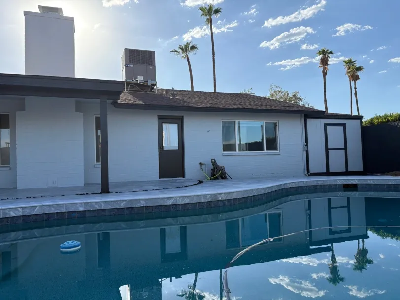 Backyard view of a modern single-story home with freshly painted exterior, featuring a swimming pool, patio area, and palm trees, highlighting a clean, refreshed residential outdoor living space.