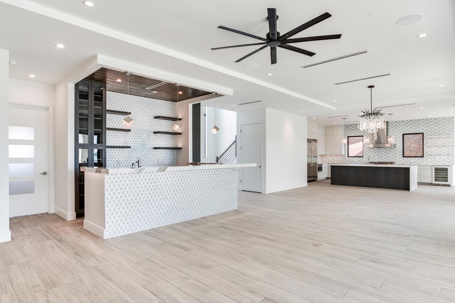Open-concept luxury home interior with a bright kitchen, large island, dining area, modern ceiling fan, and natural light throughout.