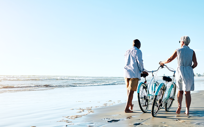 Two people pushing their bikes along the beach.