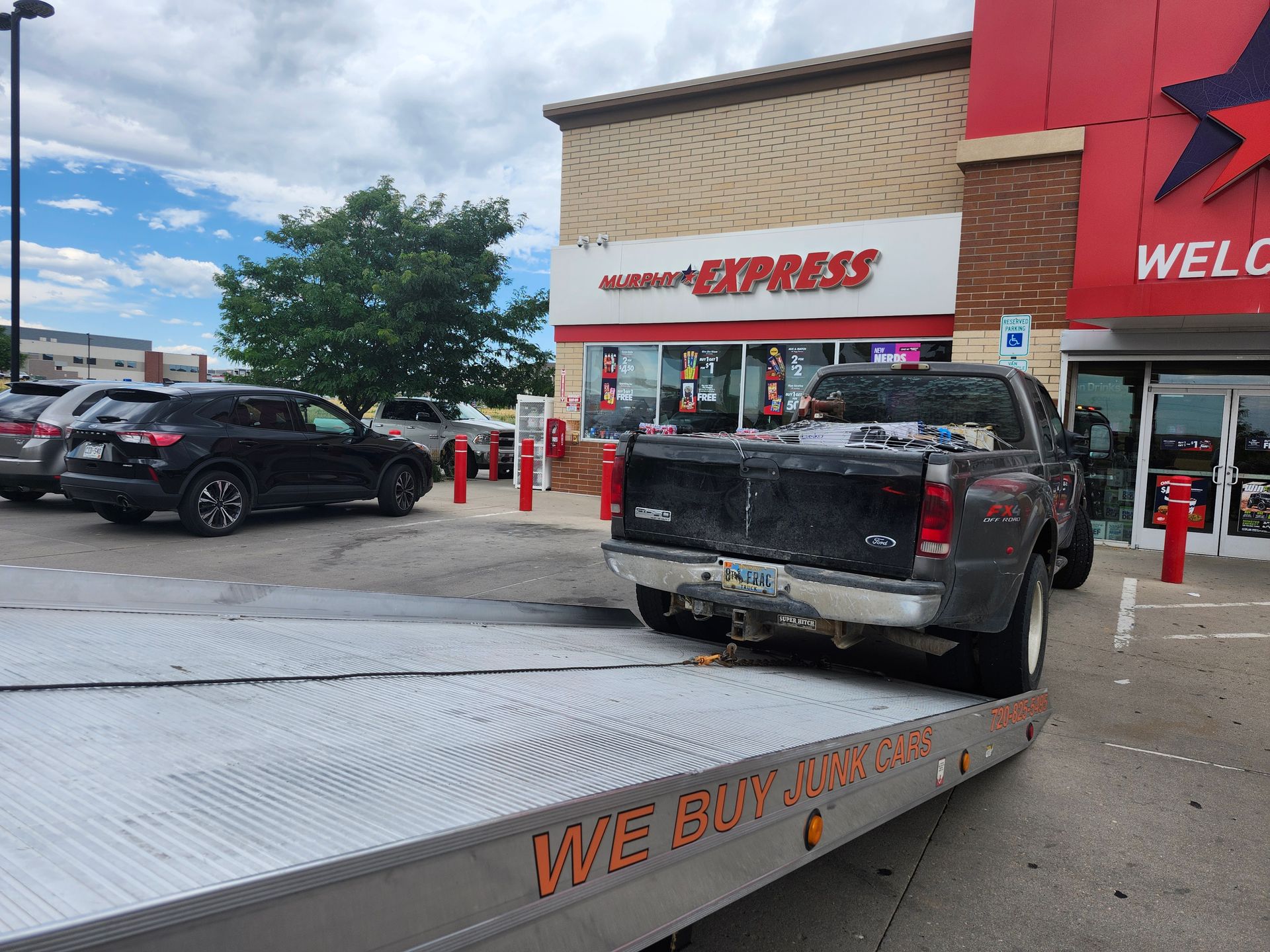 A tow truck loads a pickup truck outside a Murphy Express gas station, highlighting vehicle recovery and junk car removal services in a commercial parking lot environment.
