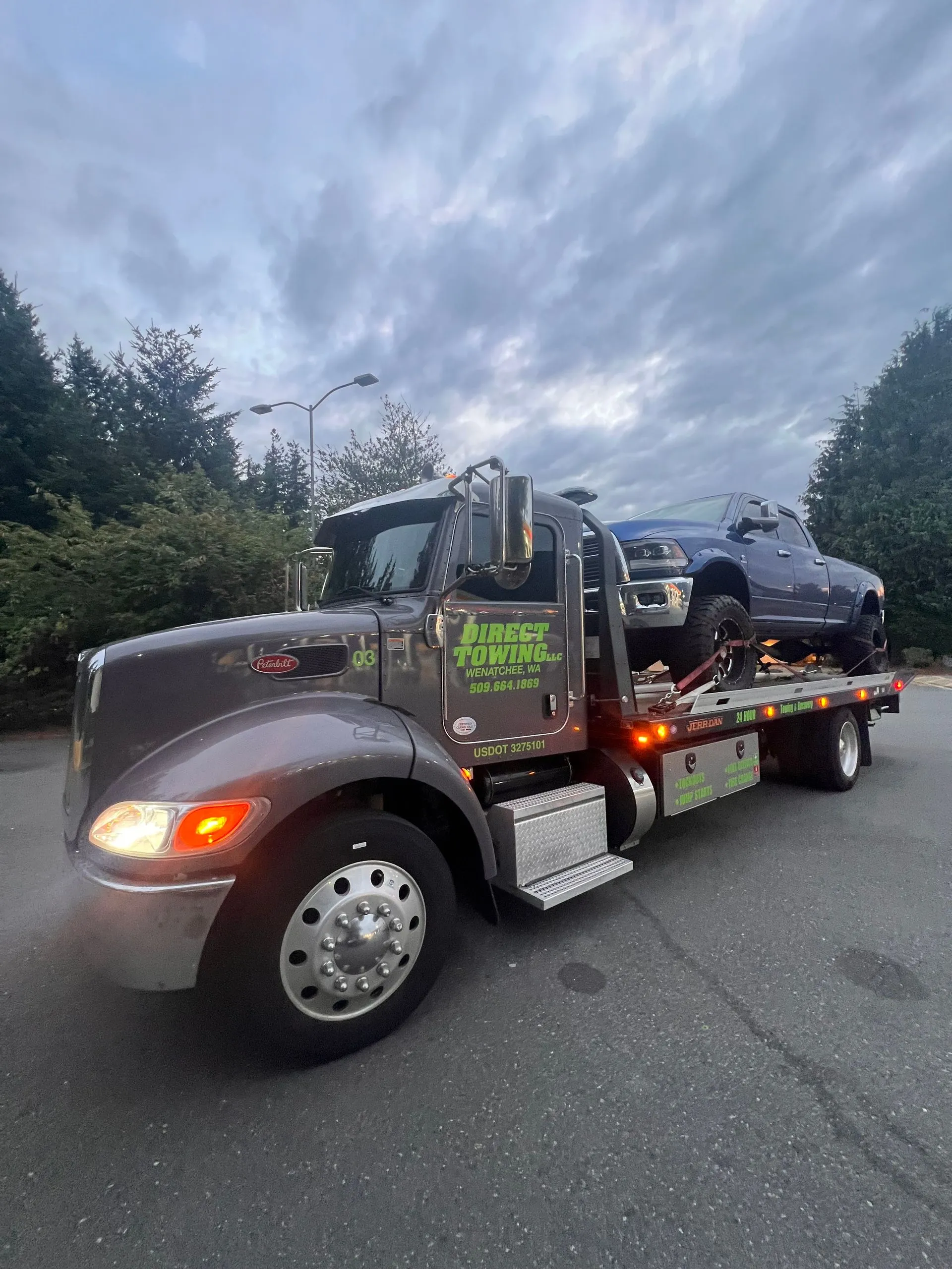Direct Towing transporting a lifted pickup truck during evening conditions, demonstrating heavy-duty towing capabilities, secure vehicle transport, professional recovery services, and reliable roadside assistance operations.