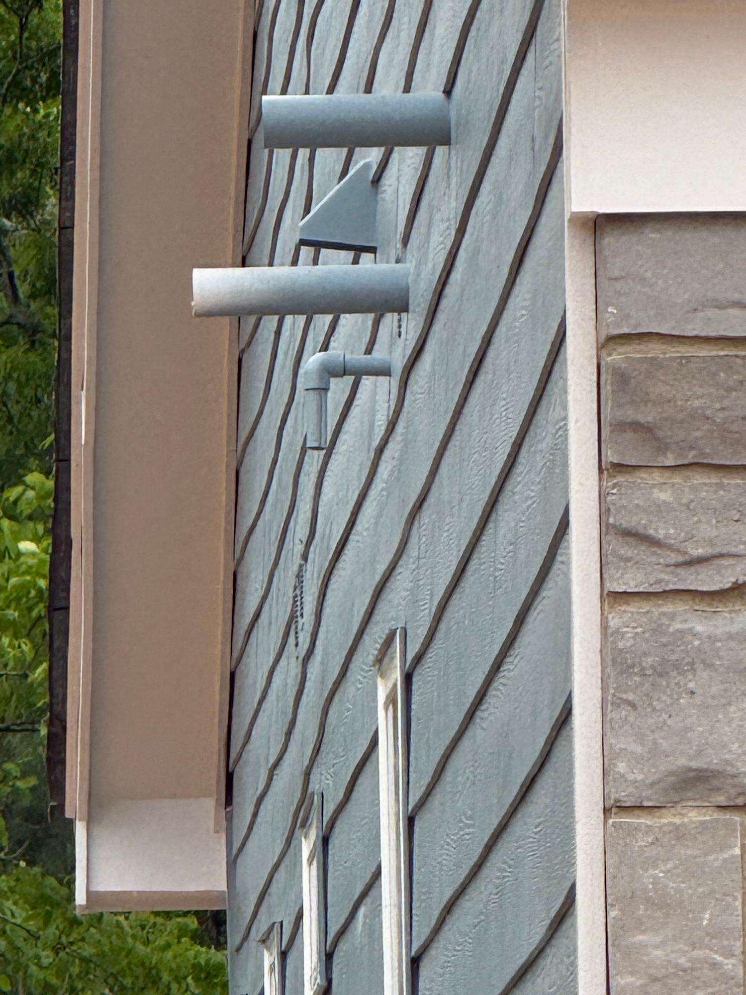 Close-up of gray lap siding on a home exterior with multiple PVC pipe penetrations and an exhaust vent.