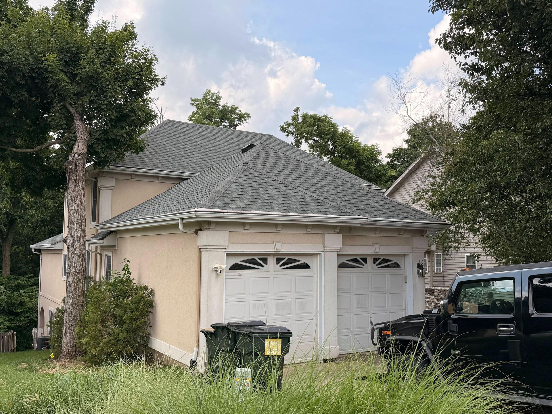 Side view of a residential home showcasing a newly completed gray asphalt shingle roof above a two-c 