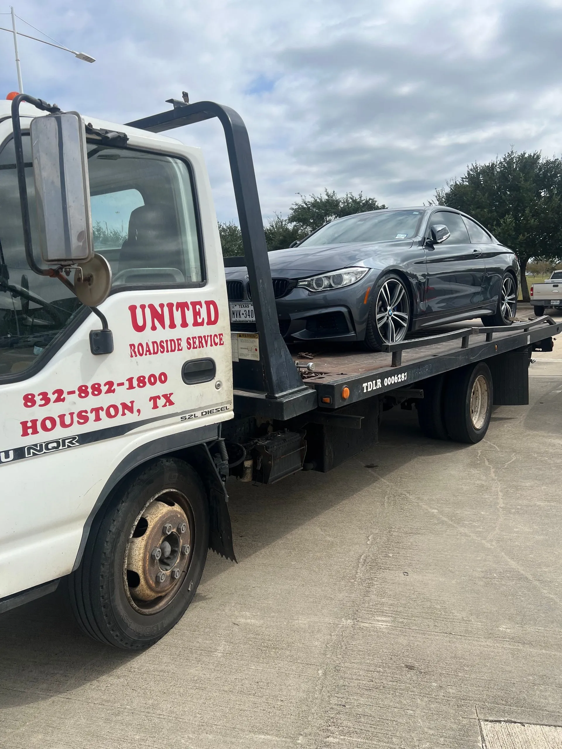 United Roadside Service securely transports a gray BMW coupe on a professional flatbed tow truck, providing safe loading, careful vehicle handling, dependable transportation, reliable roadside assistance, and expert towing services.